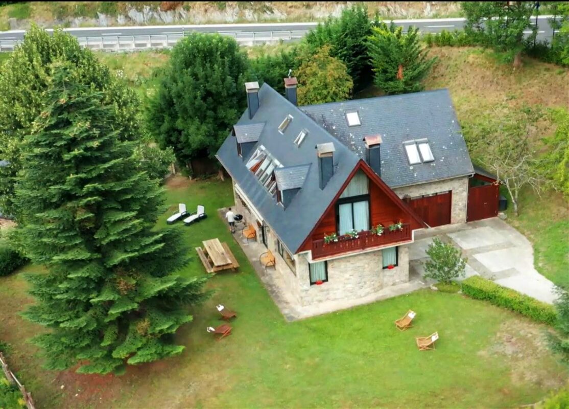 Vista aérea con dron de Casa Lola Pirene mostrando el extenso jardín privado de 400m2, la mesa de picnic y hamacas bajo el sol de Vielha, ideal para grupos de 12.