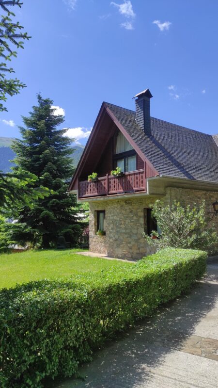 Fachada de piedra y madera de Casa Lola Pirene bajo un cielo azul despejado en primavera.