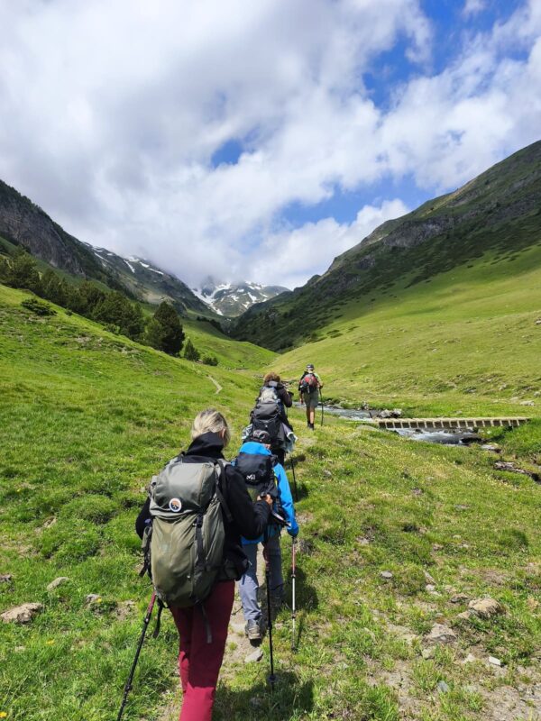 Ruta de senderismo en grupo cruzando un río en los Pirineos cerca de una casa rural en Vielha