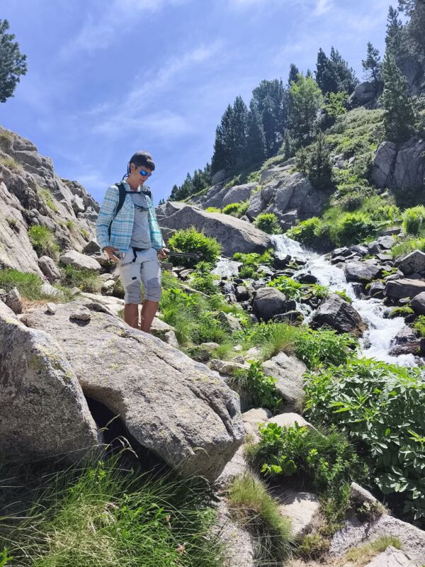 Senderista caminando junto a un arroyo de montaña en el Pirineo para turismo termico